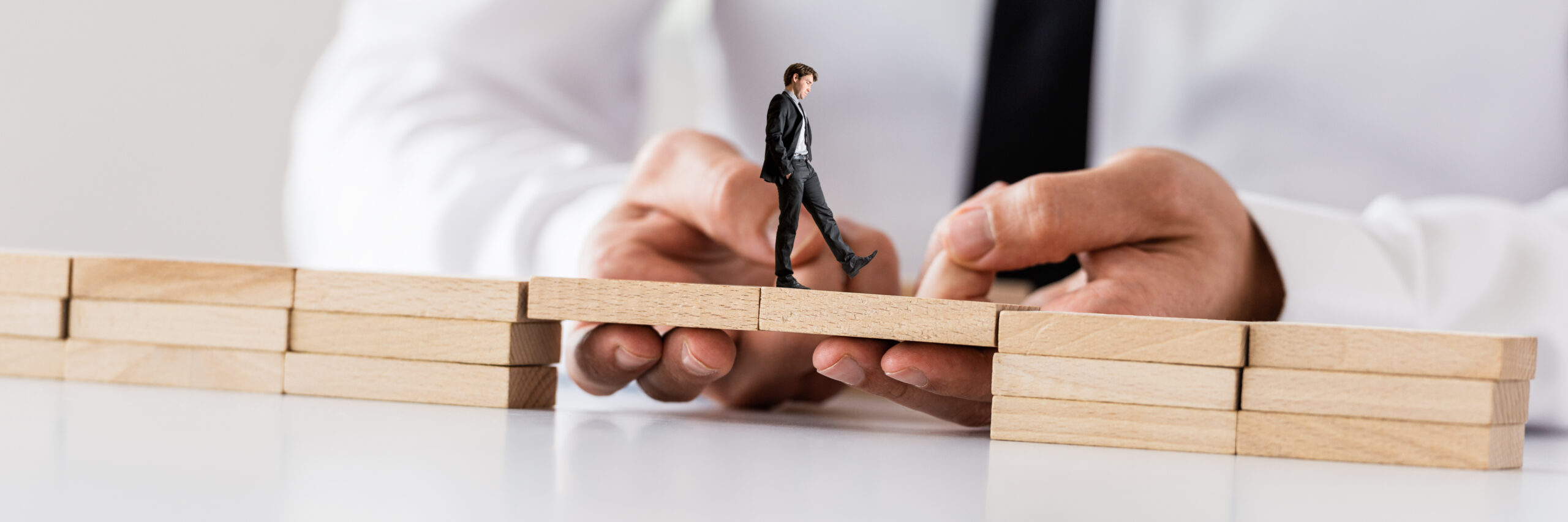 Businessman,Making,A,Bridge,Between,Two,Stacks,Of,Wooden,Pegs