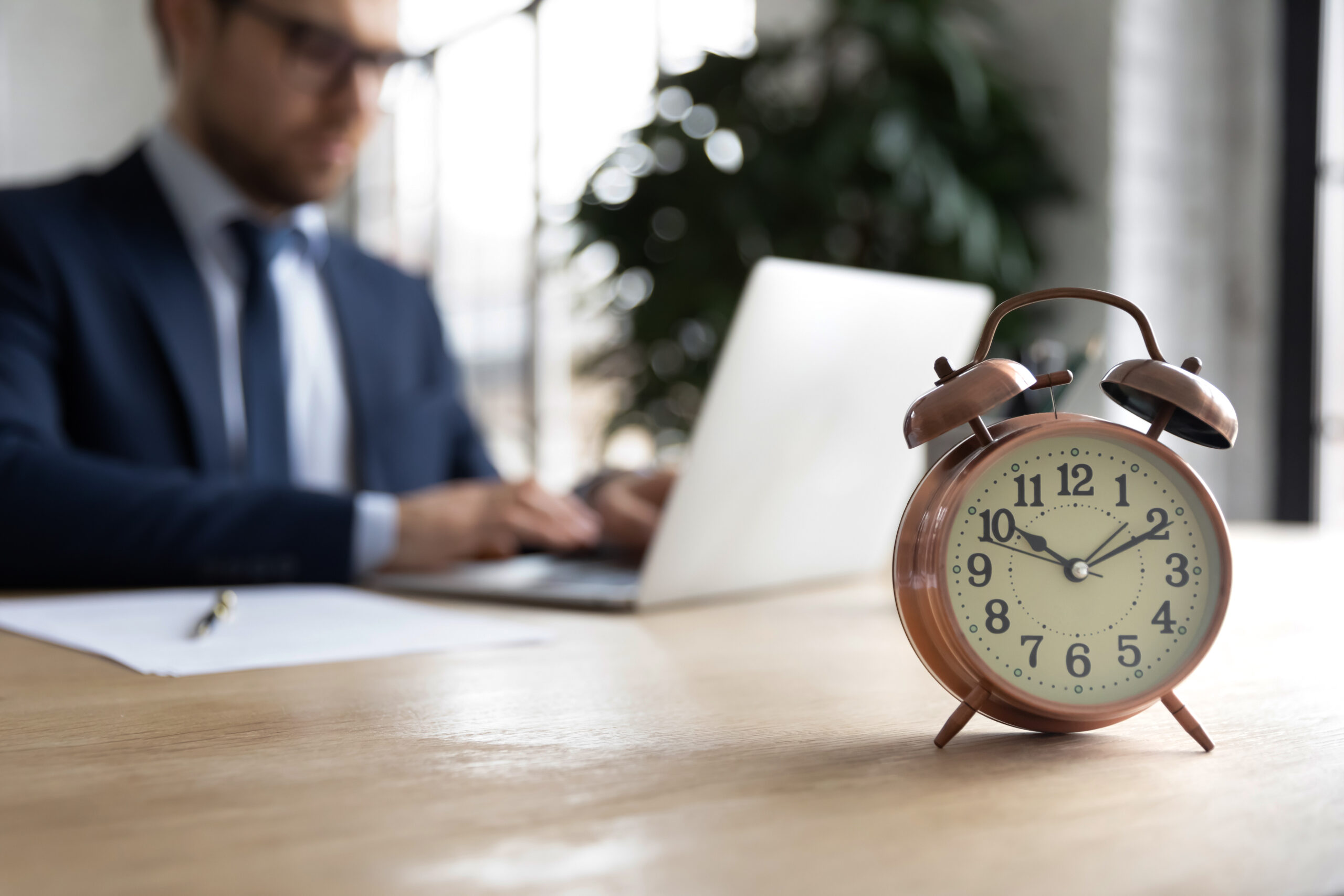 Close,Up,Of,Clock,On,Forefront,With,Businessman,Work,On