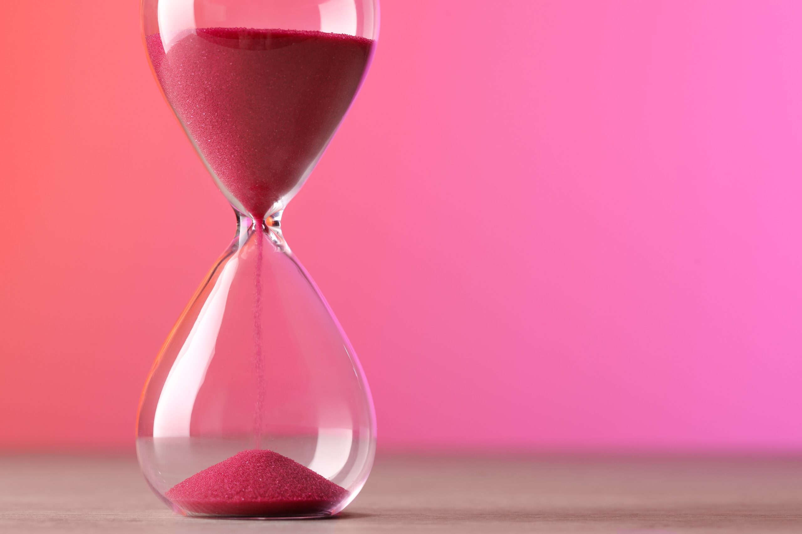 Hourglass,With,Flowing,Pink,Sand,On,Table,Against,Color,Background.